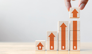 Stacked wooden blocks with dollar signs and upward arrows symbolize financial growth and profitability, showcasing the concept of increasing revenue or investment returns
