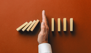 A hand stopping a row of falling dominoes, symbolizing risk management, prevention, and intervention strategies.