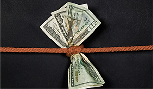 A bundle of U.S. dollar bills tied tightly with a rope, representing financial constraints, budget restrictions, or economic pressure